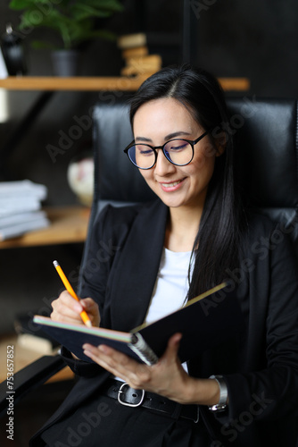 фотографія A professional Asian woman meticulously plans and writes, embodying business acumen in a modern office