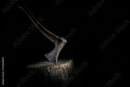 A scary rusty ax sticks out of a wooden stub log in a night photo