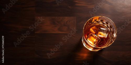 Top view of a glowing glass of whiskey or scotch on a dark wood background. Free space for advertising text of alcoholic beverages.