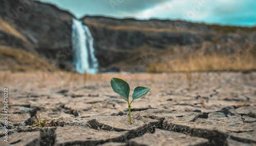 The Earth day, ecology and climate change abstract concept. A single small green plant growing in a cracked barren desert land. Waterfall in background. 