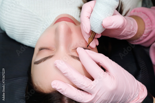 The master fingers hold the eyelid to perform permanent makeup of eyelashes. Permanent eye makeup and PMU eyelashes