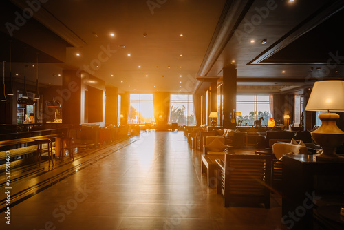 An interior view of a luxurious hotel lounge with modern furniture, large windows, and the sun setting in the background casting a warm glow. photo