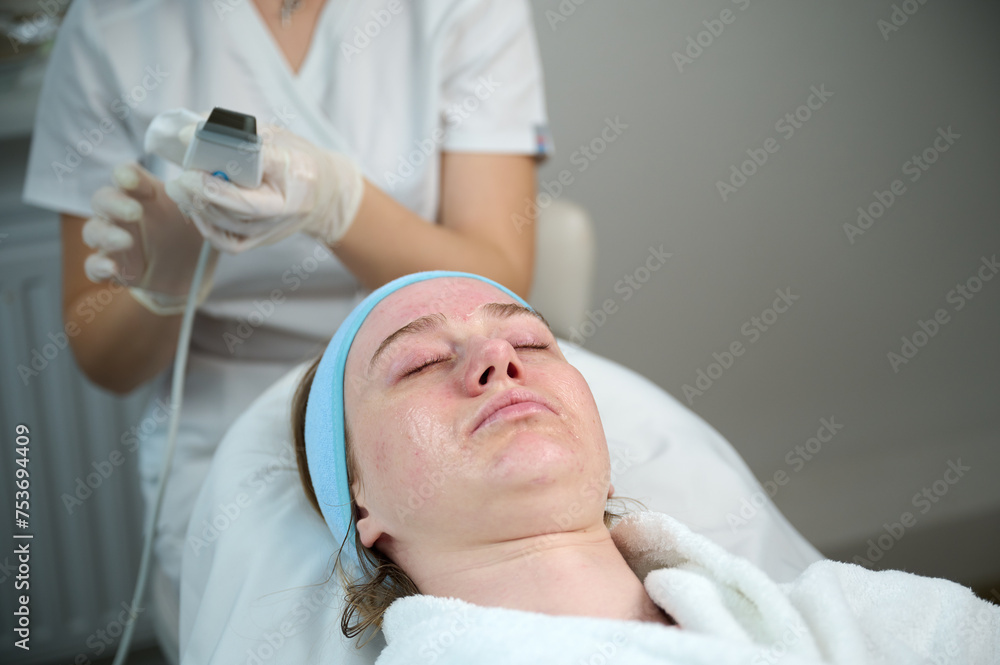Close up of ultrasound skin cleaning and facial peeling procedure in beauty clinic. Macro shot of woman under procedure of ultrasonic facial. Deep pore cleansing treatment Close up of ultrasound skin cleaning and facial peeling procedure in beauty clinic. Macro shot of woman under procedure of ultrasonic facial. Deep pore cleansing treatment