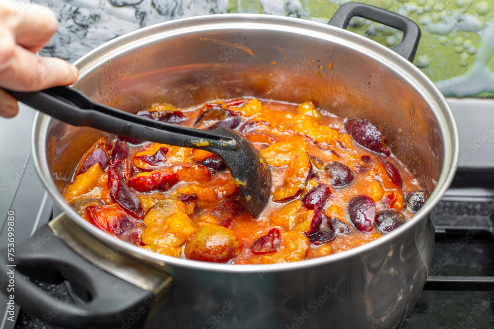 woman makes jam from ripe plums, stirring them in a saucepan. Canning berries and fruits