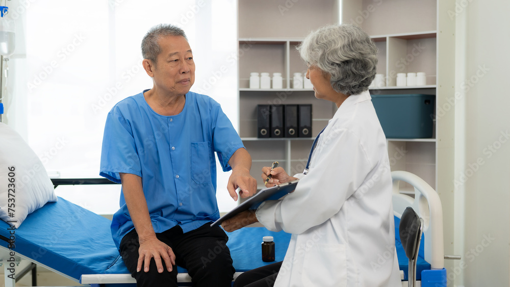 Fototapeta premium Senior Asian female nurse doctor visits a senior patient sitting on a patient's bed, explaining, talking to a patient, helping prescribe medication, health care clinic, medical consultant concept