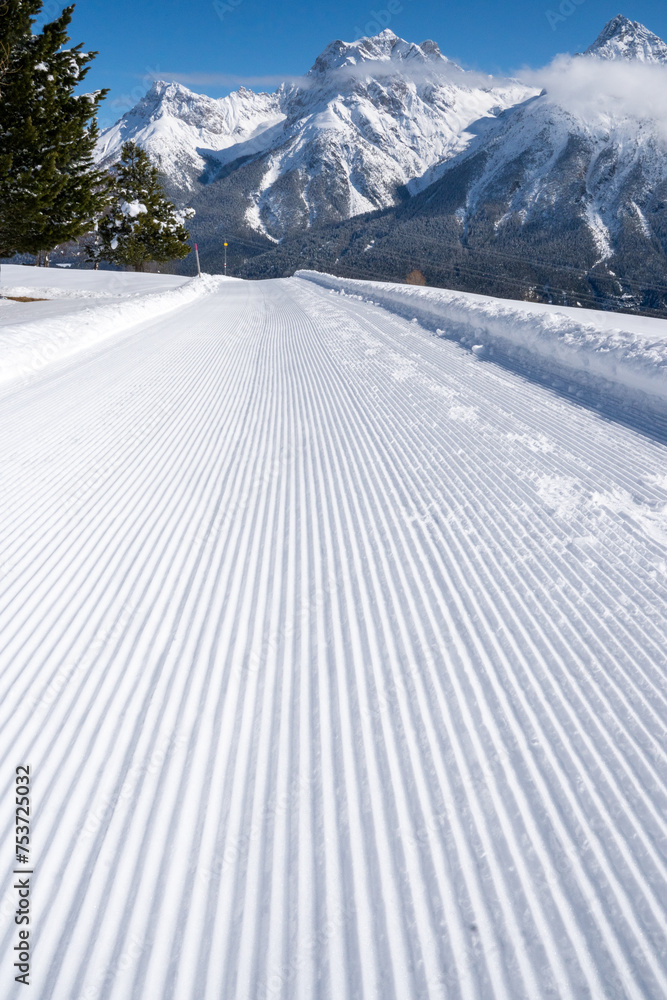 Grooves of a machine-groomed winter hiking trail in front of snow-covered mountain peaks and a blue sky in the Engadine, Switzerland Grooves of a machine-groomed winter hiking trail in front of snow-covered mountain peaks and a blue sky in the Engadine, Switzerland