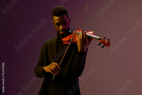 Elegant violinist in black suit performing classical music on purple background, creative musical performance concept photo