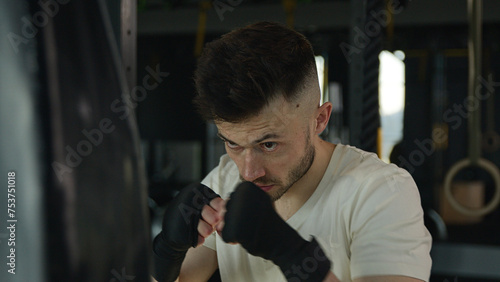 Active motivated sportsman male professional fighter boxer training boxing with punching bag in gym tired man Caucasian guy wipe sweat box workout in sport club training power hit punch beating fight