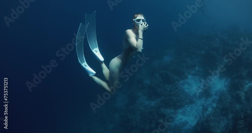 Woman freediver dives to the deep in blue ocean and equalizes pressure. photo