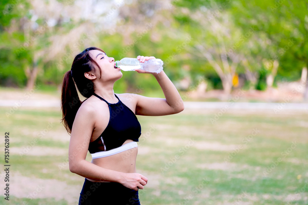 Woman hydrating post-workout in a park amidst greenery, embodying fitness and health. Teenage woman drinking water from a water bottle. Beautiful girl in black exercise clothes. Woman hydrating post-workout in a park amidst greenery, embodying fitness and health. Teenage woman drinking water from a water bottle. Beautiful girl in black exercise clothes.