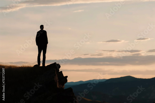 Silhouetted man standing atop a cliff overlooking a mountainous landscape at dusk