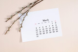 Flat lay, top view of paper desk calendar for March 2024, willow plant branches on isolated pastel beige background
