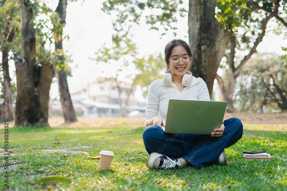 A woman is sitting on the grass with a laptop in front of her A woman is sitting on the grass with a laptop in front of her