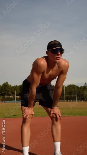 Portrait of an athlete resting on his knees after a hard training session on an athletics track. He is taking deep breaths due to fatigue. Vertical video. Concept of sacrifice and effort