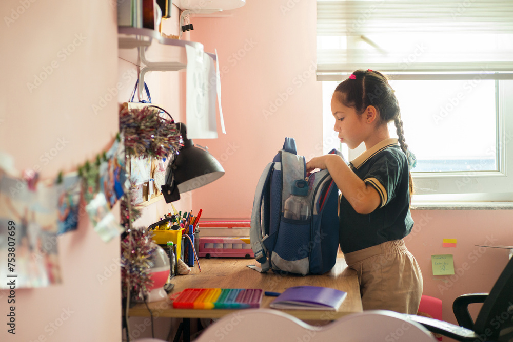 A little schoolgirl packs her backpack with her textbooks A little schoolgirl packs her backpack with her textbooks