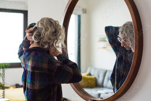 Woman fixing her hair in front of mirror before going out photo