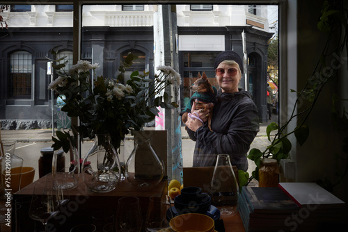 Woman looking through shop window, holding tiny dog photo