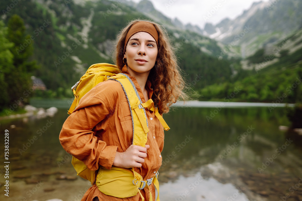 Active woman with a yellow hiking backpack traveling along hiking trails in the mountains among forests and cliffs. Concept of trekking, active lifestyle. Adventures.