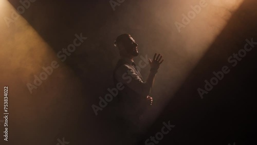 Male musician with trendy haircut stretching hand while singing song in dramatical foggy atmosphere. Skilled actor performing part in play while gesturing and creating mystical effect on stage. photo