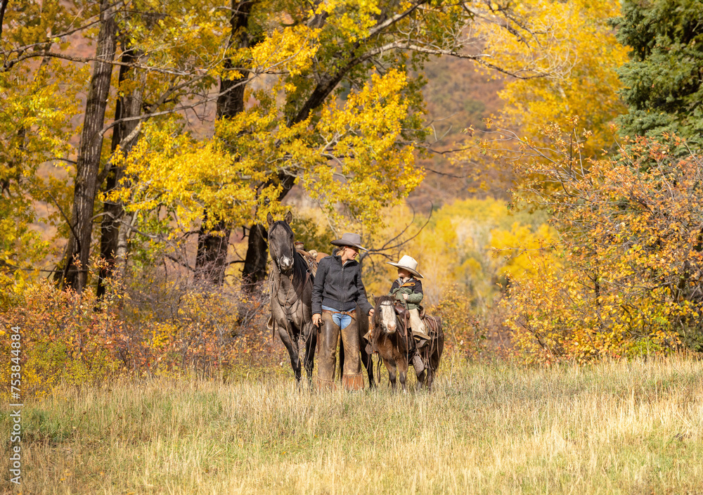 Fototapeta premium Ranch family brother and sister riding horses near cottonwoods in the fall