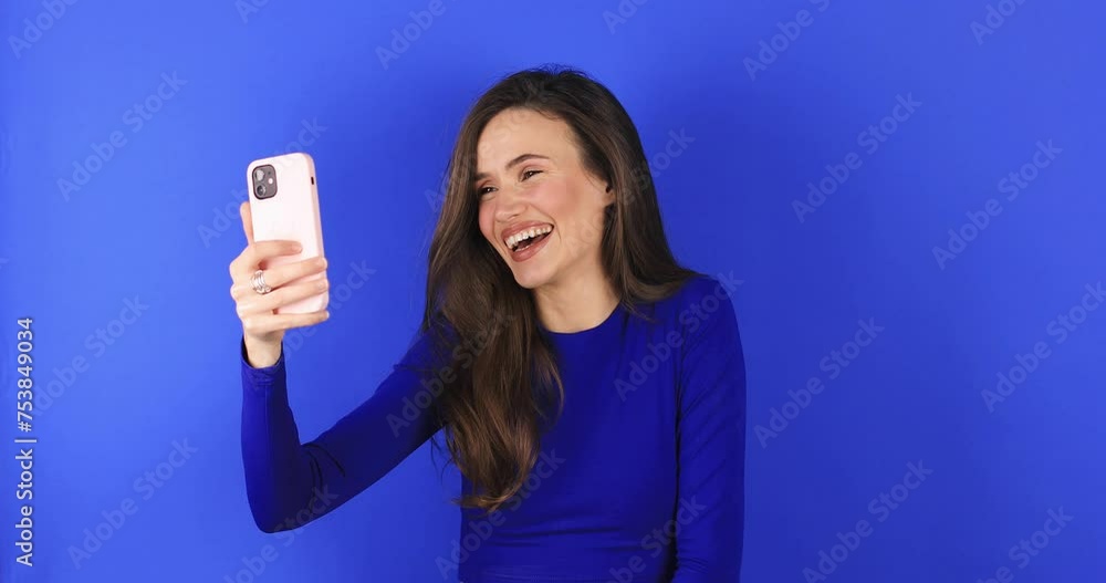 Happy brunette woman having mobile video call, wave hands and say hi, hello isolated on blue background. Nice to see you. Happy emotions. Beautiful young girl speaking video call online smartphone. Happy brunette woman having mobile video call, wave hands and say hi, hello isolated on blue background. Nice to see you. Happy emotions. Beautiful young girl speaking video call online smartphone.