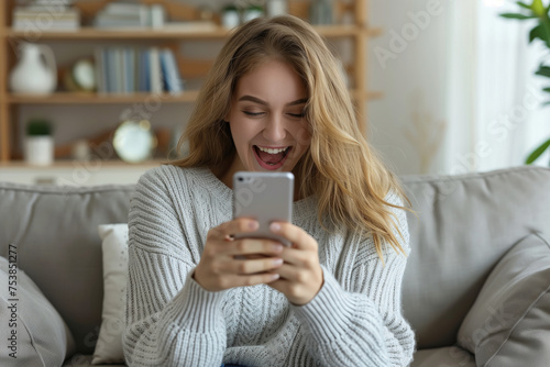 Happy excited young woman relaxing on couch using mobile phone winning in online app game. Young lucky girl feeling winner looking at cellphone, receiving great news or discount offer