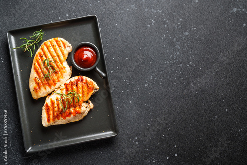 Grilled meat. Chicken steak with spices and ketchup. Top view on black table.