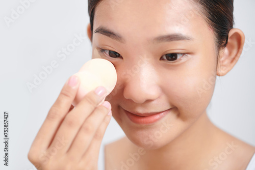 Charming girl applying foundation on her face using makeup sponge photo