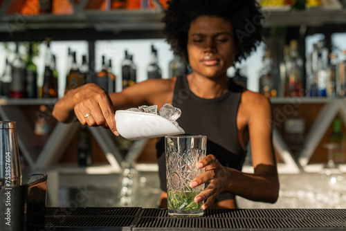 Black female bartender putting ice in a glass while preparing a  photo