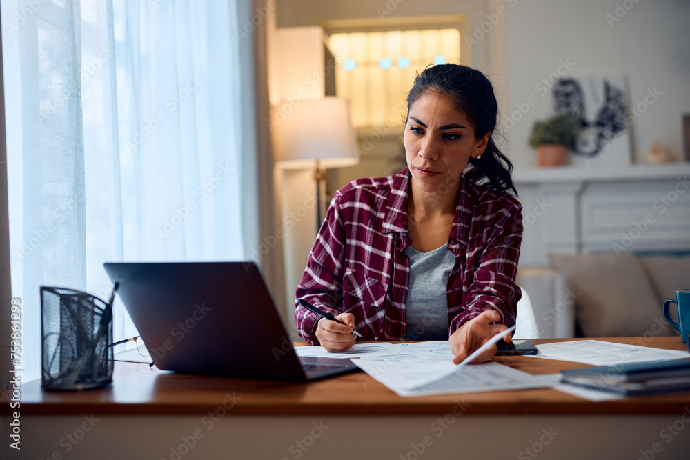Latin American woman using laptop while working on documents at home. Latin American woman using laptop while working on documents at home.