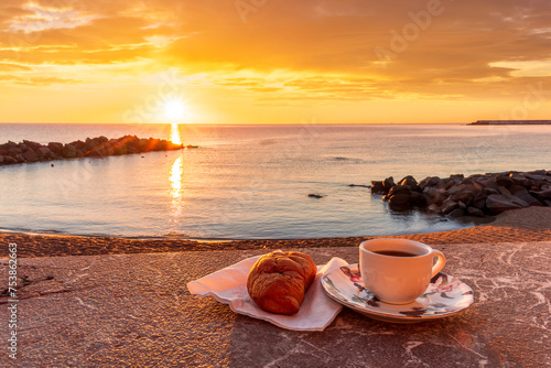 cup of coffee or tea with croissant on a morning embarkment beach with blue sea and beautiful cloudy sunrise or sunset on background  street food breakfast concept