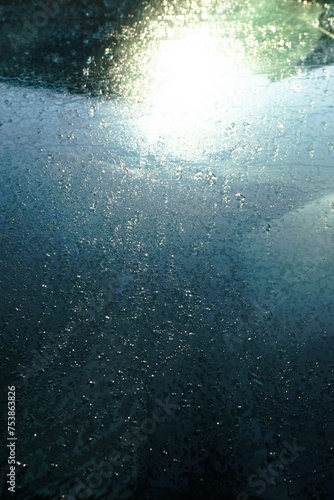 Abstraktes Motiv mit Eismuster auf Glasscheibe mit weißer Sonnenreflexion bei Sonne, Frost und Kälte am Morgen im Winter