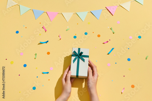 Woman holding gift box with green bow on light yellow background photo