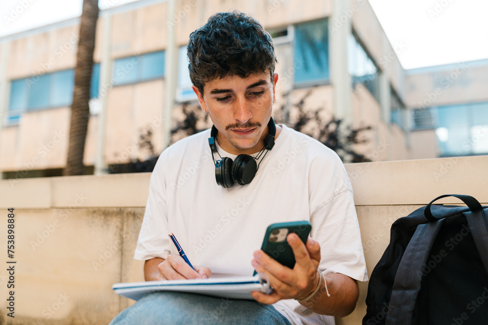 Student using cellphone while taking notes in campus Student using cellphone while taking notes in campus