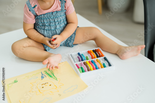Little baby girl holding wax crayons and drawing first scratches