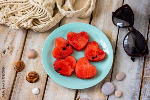 Summer flat lay. Watermelon hearts on a blue plate on wooden background. Sun glasses, shells, sea stones. Vacation mode, holiday inspiration, travelling concept