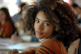 Young student with curly hair and striped top looks over her shoulder in a lively classroom.