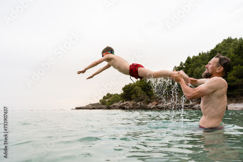 Father throws his little son in the sea water photo