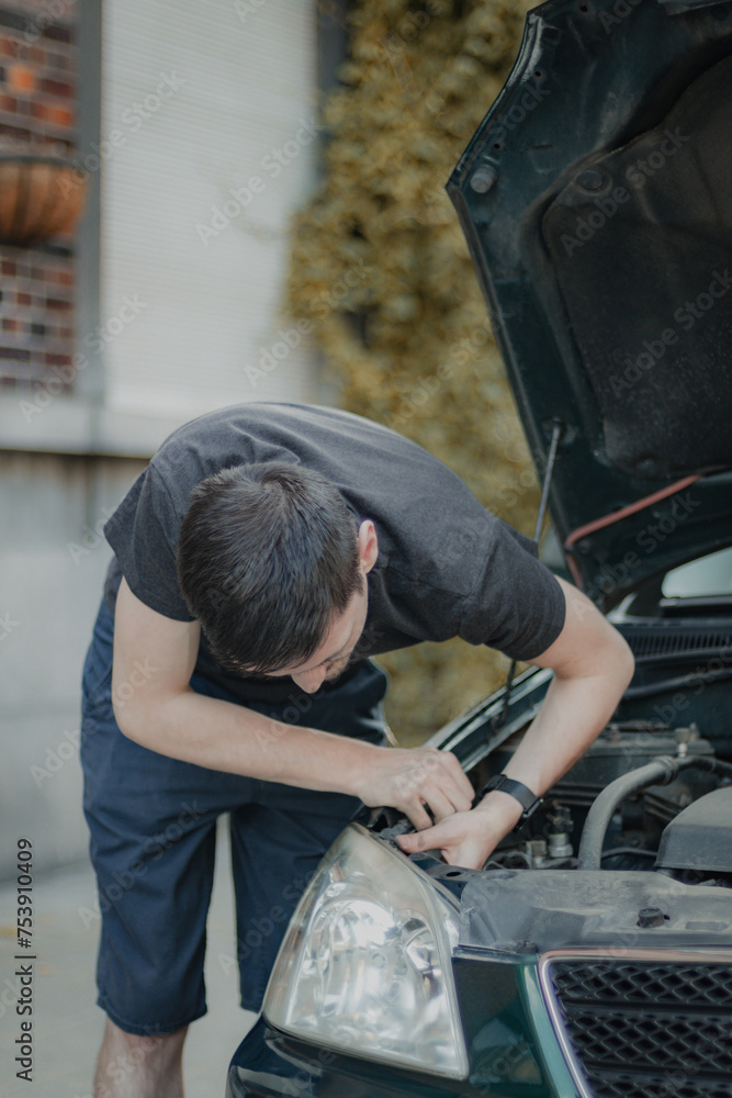 A young man unscrews a headlight bulb inside the hood. A young man unscrews a headlight bulb inside the hood.