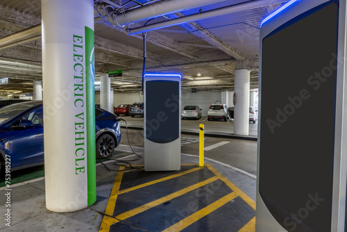 Electric vehicle charging station at parking structure has one car charging and one open stall for renewable energy. © motionshooter