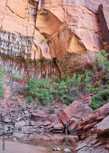 Man at the foot of a large rock wall in Zion National Park photo