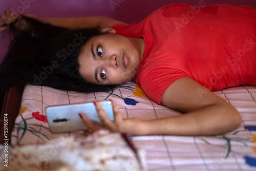 Young girl browsing smartphone lying on bed inside home photo