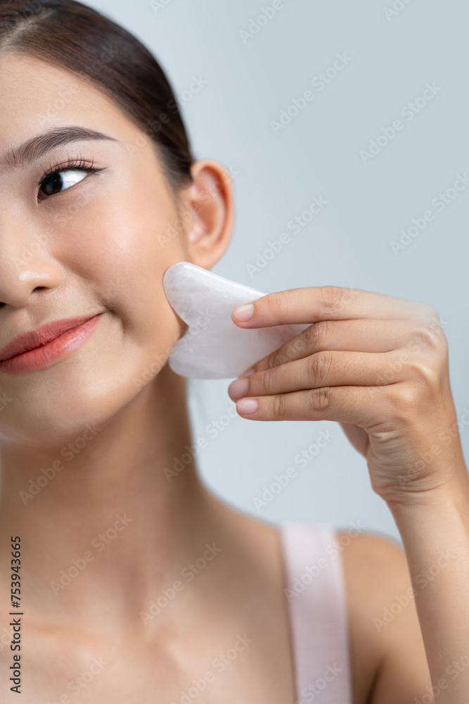Young female massaging face by gua sha quartz stone scraper Young female massaging face by gua sha quartz stone scraper
