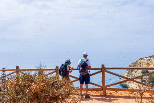 Couple of mid age Tourists with backpacks enjoying the view of the sea from the top. Benagil, Carvoeiro, Algarve, Portugal.
