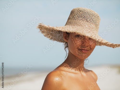 Beach sun hat woman on vacation. Close-up of a girl's face in straw sunhat enjoying the sun looking at the camera.