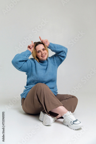 Funny young plus size woman sitting on floor against gray backdrop photo