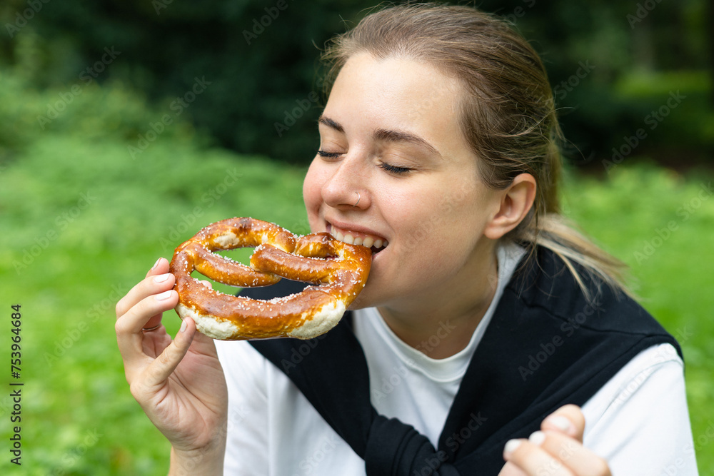 Young happy woman eating a german pretzel in the park Young happy woman eating a german pretzel in the park