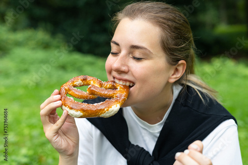 Young happy woman eating a german pretzel in the park photo
