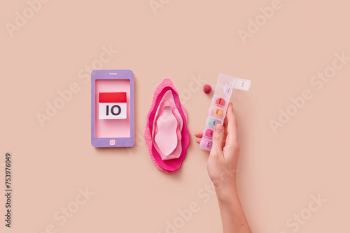 Female hand holding pill box near decorative vagina and smartphone photo
