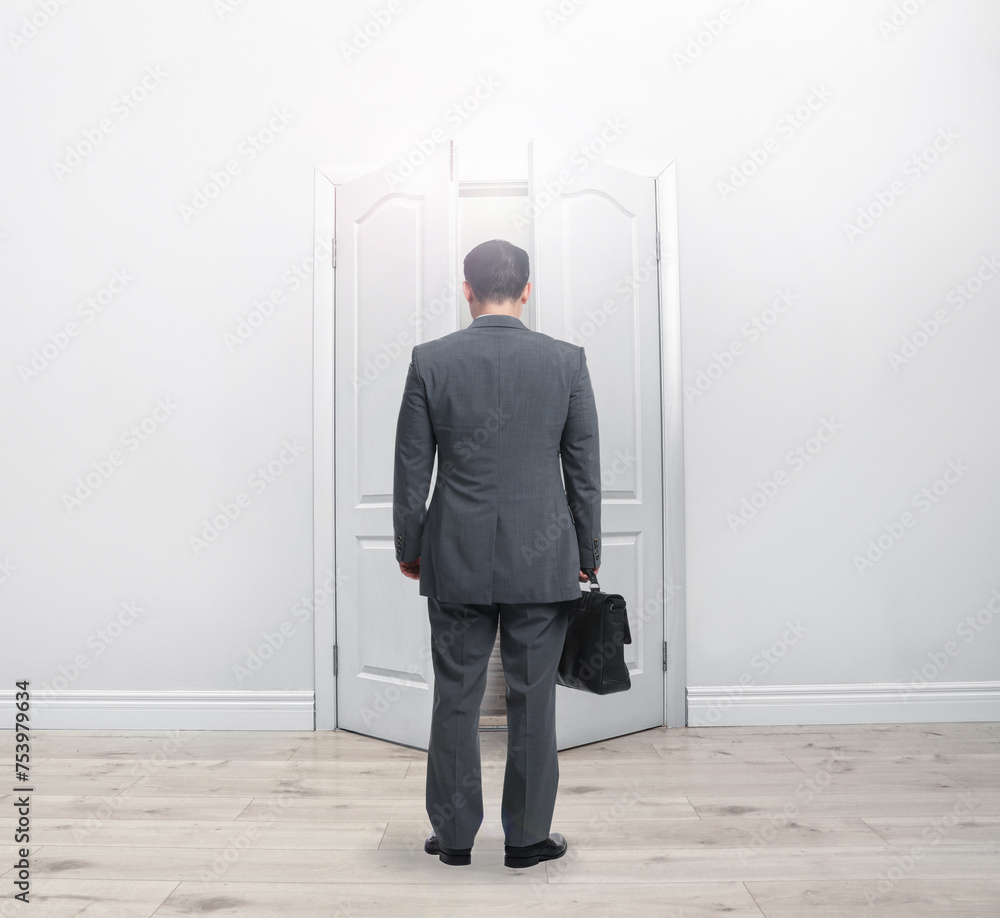 Man with briefcase standing in front of open door, back view